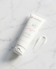 A white tube of Silverrette silky touch zinc cream for sensitive skin, placed diagonally on a white marble surface next to a smear of the white cream.